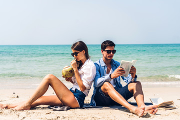 Fototapeta premium Young couple drinking coconut juice and reading a book on the tropical beach.Couple relaxing on the beach.Summer vacations