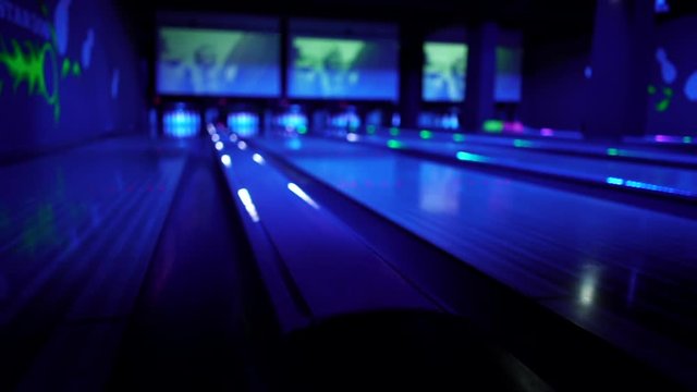 A bowling ball traveling down the lane and hitting pins at a Black Light UV Bowling alley.