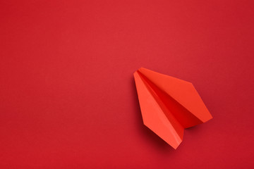 Flat lay of red paper plane on red background with text space.