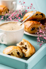 Holiday break with cup of coffee, mini fresh croissants chocolate bun and carnation flowers on turquoise background.