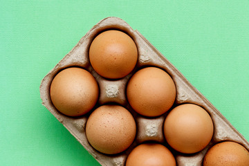 Brown hen eggs in a cardboard carton with a green background.