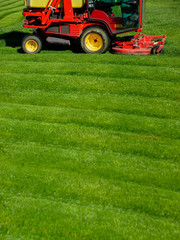 Bright red lawn mower on a freshly cut green grass mowing