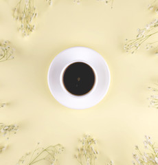 A cup of black coffee on a yellow background with gypsophila branches.