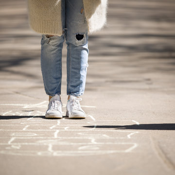 Closeup of the feet of a girl playing hopscotch, painted on asphalt. Games for children in the fresh air. The concept of fun for adults and childrens on summer holidays.
