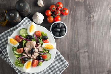 Fresh Caesar tuna salad with delicious tuna fish, ruccola, spinach, cabbage, arugula, egg, parmesan and cherry tomato on wooden background. Oil, salt and pepper. Healthy and diet food concept.
