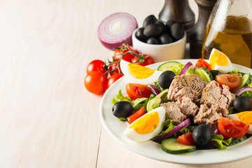 Fresh Caesar tuna salad with delicious tuna fish, ruccola, spinach, cabbage, arugula, egg, parmesan and cherry tomato on wooden background. Oil, salt and pepper. Healthy and diet food concept.