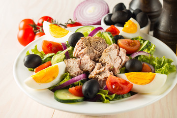 Fresh Caesar tuna salad with delicious tuna fish, ruccola, spinach, cabbage, arugula, egg, parmesan and cherry tomato on wooden background. Oil, salt and pepper. Healthy and diet food concept.