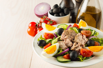 Fresh Caesar tuna salad with delicious tuna fish, ruccola, spinach, cabbage, arugula, egg, parmesan and cherry tomato on wooden background. Oil, salt and pepper. Healthy and diet food concept.