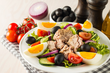 Fresh Caesar tuna salad with delicious tuna fish, ruccola, spinach, cabbage, arugula, egg, parmesan and cherry tomato on wooden background. Oil, salt and pepper. Healthy and diet food concept.