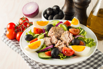 Fresh Caesar tuna salad with delicious tuna fish, ruccola, spinach, cabbage, arugula, egg, parmesan and cherry tomato on wooden background. Oil, salt and pepper. Healthy and diet food concept.