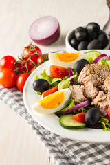 Fresh Caesar tuna salad with delicious tuna fish, ruccola, spinach, cabbage, arugula, egg, parmesan and cherry tomato on wooden background. Oil, salt and pepper. Healthy and diet food concept.