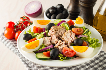Fresh Caesar tuna salad with delicious tuna fish, ruccola, spinach, cabbage, arugula, egg, parmesan and cherry tomato on wooden background. Oil, salt and pepper. Healthy and diet food concept.
