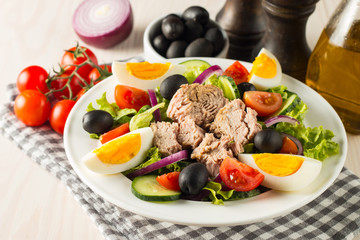 Fresh Caesar tuna salad with delicious tuna fish, ruccola, spinach, cabbage, arugula, egg, parmesan and cherry tomato on wooden background. Oil, salt and pepper. Healthy and diet food concept.