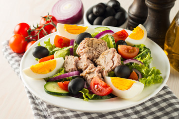 Fresh Caesar tuna salad with delicious tuna fish, ruccola, spinach, cabbage, arugula, egg, parmesan and cherry tomato on wooden background. Oil, salt and pepper. Healthy and diet food concept.