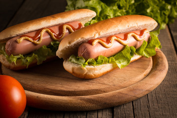 Photo of barbecue grilled hot dog with yellow mustard and ketchup on wooden background. Hot dog sandwich with potato fries and sauces.