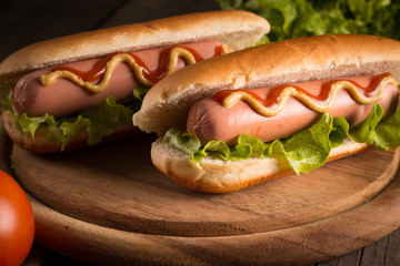Photo of barbecue grilled hot dog with yellow mustard and ketchup on wooden background. Hot dog sandwich with potato fries and sauces.