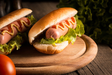Photo of barbecue grilled hot dog with yellow mustard and ketchup on wooden background. Hot dog sandwich with potato fries and sauces.
