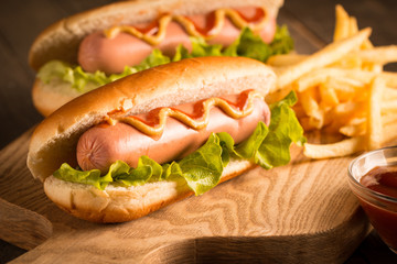 Photo of barbecue grilled hot dog with yellow mustard and ketchup on wooden background. Hot dog sandwich with potato fries and sauces.