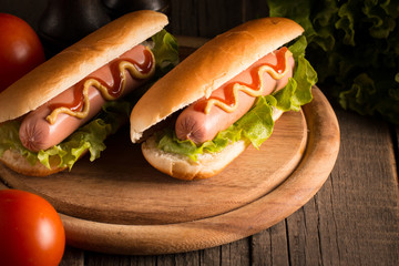 Photo of barbecue grilled hot dog with yellow mustard and ketchup on wooden background. Hot dog sandwich with potato fries and sauces.
