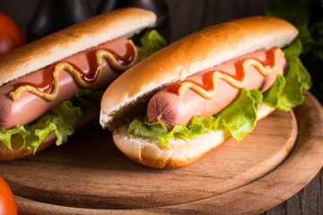 Photo of barbecue grilled hot dog with yellow mustard and ketchup on wooden background. Hot dog sandwich with potato fries and sauces.