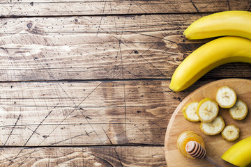 Banana and sliced banana into pieces with honey on wooden background, copy space.