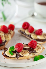 Light summer breakfast or lunch with sandwiches of white bread with chocolate paste, bananas and raspberries on the background of the village table