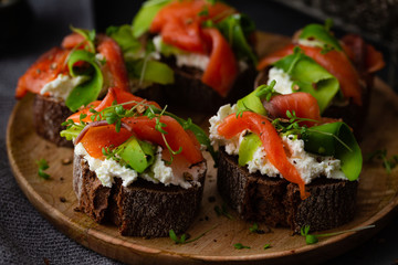 Homemade toast sandwich with rye bread, salmon, avocado, cottage cheese and microgreen sprouts on dark board background. healthy food - breakfast close-up