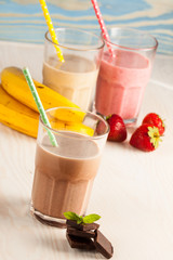 Long glasses of milkshakes with chocolate, strawberry, banana, with ice cream on white and blue background. Shakes and smoothies. Milk shake and cocktail for summer.