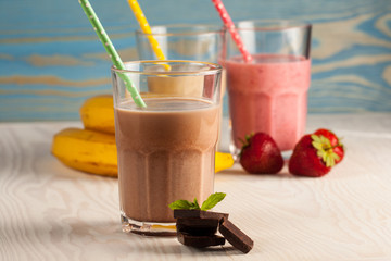 Long glasses of milkshakes with chocolate, strawberry, banana, with ice cream on white and blue background. Shakes and smoothies. Milk shake and cocktail for summer.
