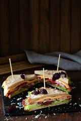 A club sandwich on a dark table with ham, cheese, bacon and lettuce.
