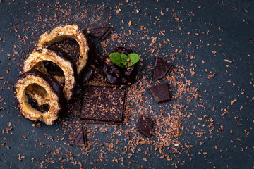 Top view on pieces of a chocolate cake and chocolate with mint leaf on a dark background