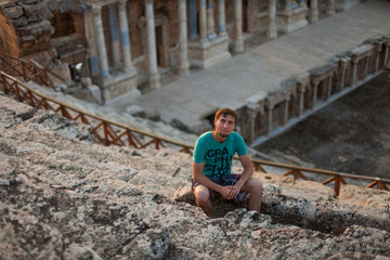 Men sitting on the steps of the ancient amphitheater Beautiful young men traveler admiring the view. Tourist watching on ruins of theater in ancient Hierapolis, now Pamukkale, Turkey