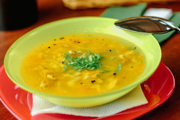 Chicken soup in a green plate over the wooden table on cafe.
