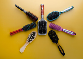 Various colored brushs and combs for hair on yellow background.