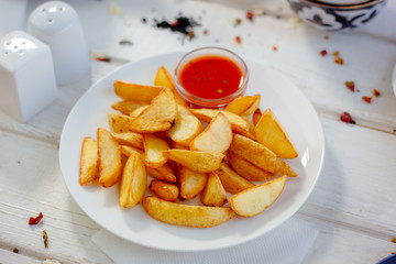 Fried potatoes with red tomato sauce on the white plate.