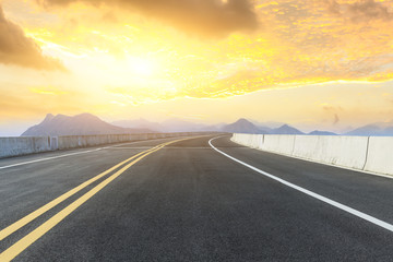 Empty asphalt road and mountains with beautiful clouds at sunset
