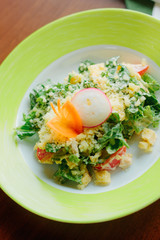 Salad with radish, carrot, lettuce and cheese in a green plate.