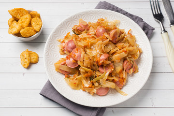 Stewed cabbage with sausages in a plate on the table. Selective focus.