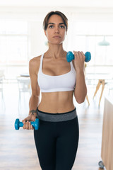 Sporty young woman lifting dumbbells at home.