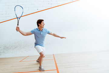 Emotional sportsman in blue polo shirt playing squash in four-walled court