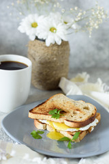Egg toasts with fresh greens and coffee for breakfast on a gray concrete background and a vase of flowers