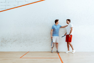 Full length view of squash player putting hand on shoulder of friend
