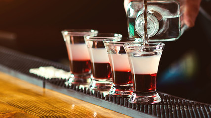 Bartender pouring strong alcoholic drink into small glasses on bar. Red shots at the nightclub....