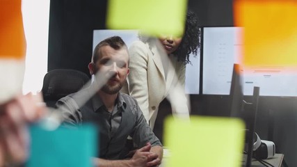 international teamwork in modern office, man and women managers look at the board with sticky notes, women draws arrows infographic on the glass. - Powered by Adobe
