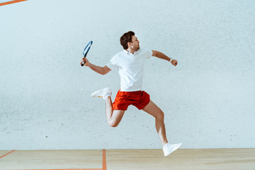 Sportsman in polo shirt jumping while playing squash in four-walled court