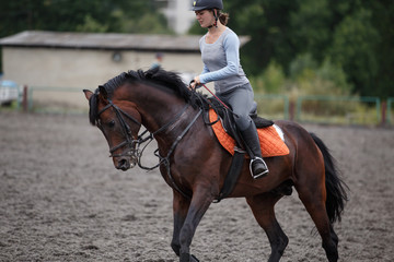 Young girl riding bay horse on equestrian sport training
