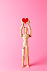 The mannequin is holding a heart. Wooden mannequin holds heart in his hands. Wooden mannequin. Wooden man.