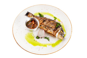 Plate of grilled dorado fish served with sauce isolated at white background.