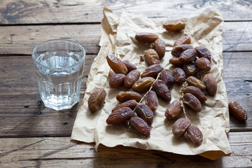 Dried dates fruits on a branch and a glass of water on a wooden table. Traditional fast breaking, Muslims evening meal during holy Ramadan