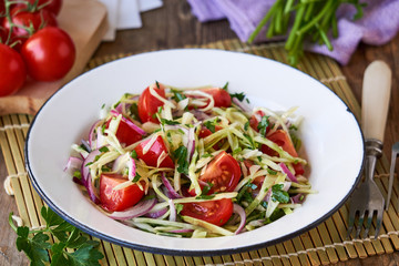 Vegetable salad with cherry tomatoes, cabbage and red onions in a white bowl